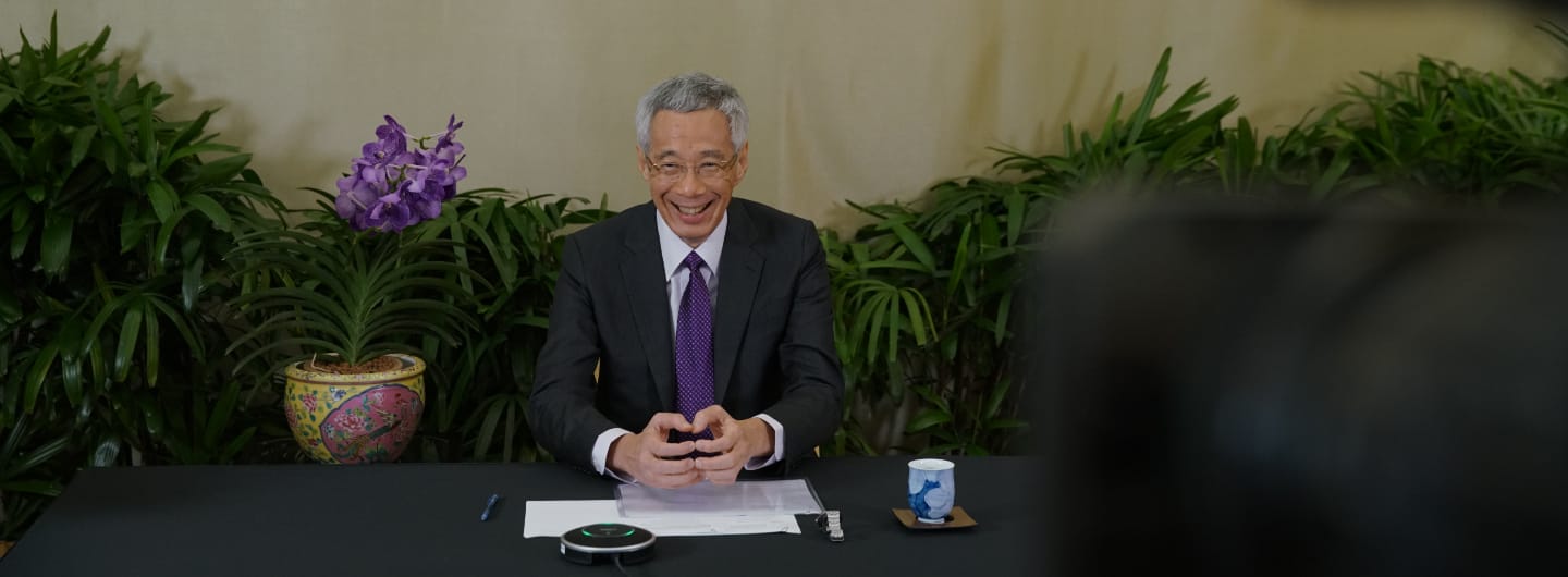 Lee Hsien Loong in a suit at a desk, with plants and a purple orchid.